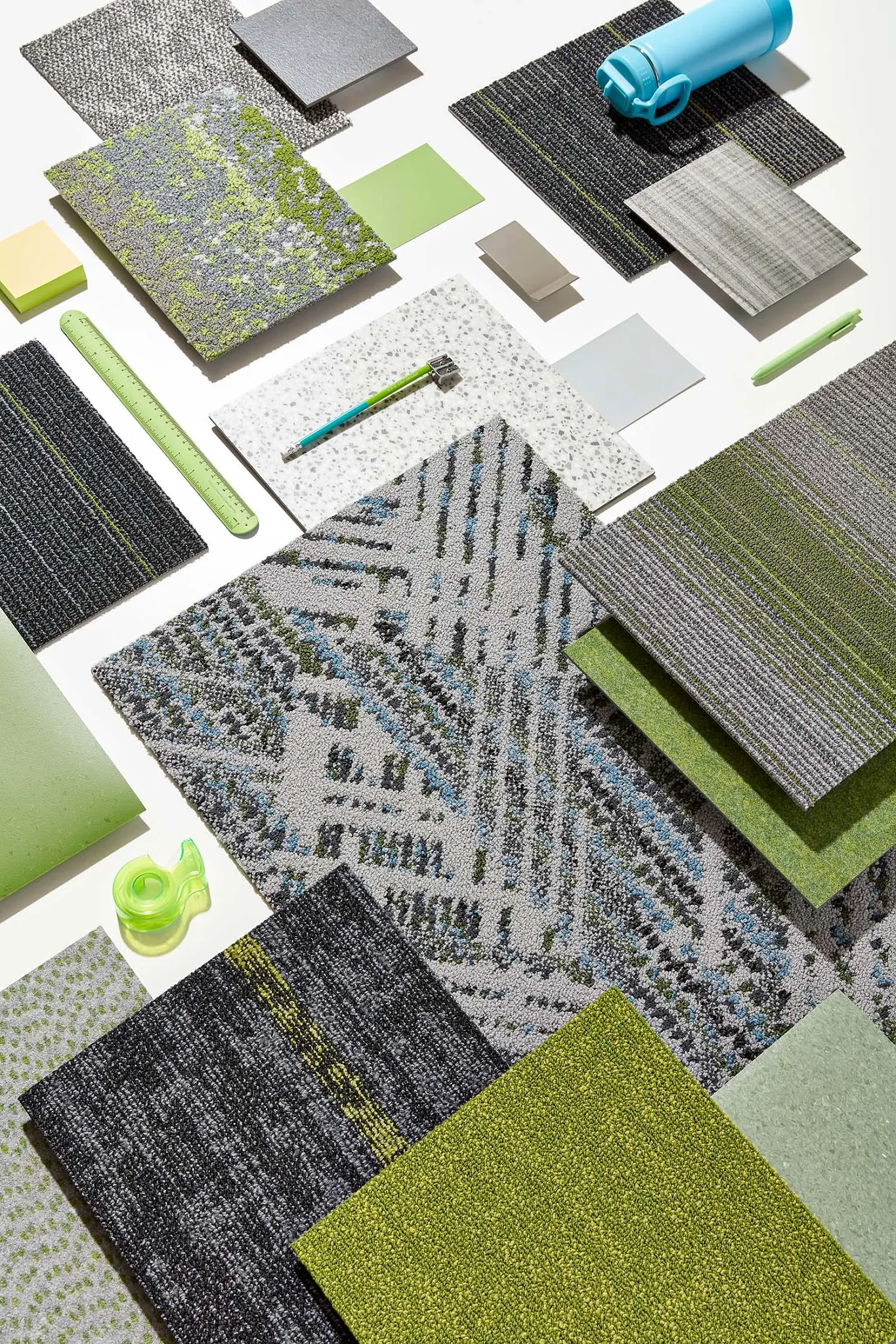 Assorted commercial carpet tile swatches in shades of green, gray, and blue with various textures and patterns