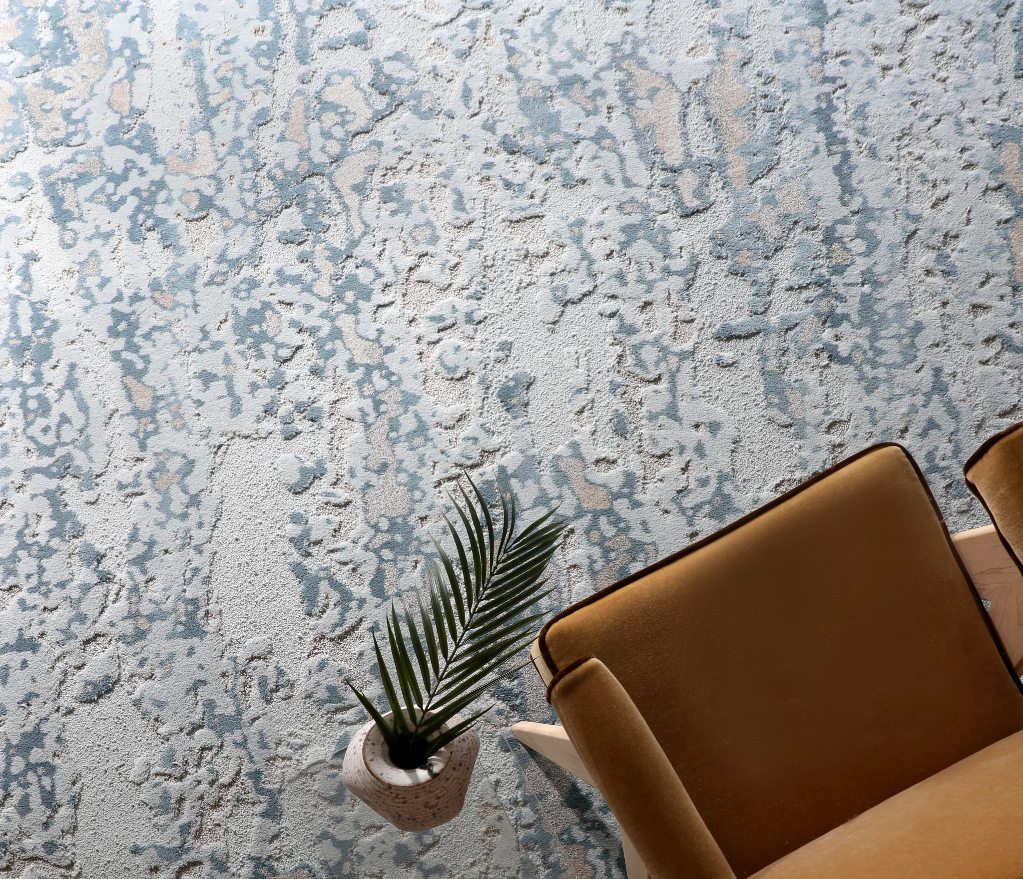 Elegant blue and gray patterned carpet flooring in a modern living room with a tan leather chair and decorative plant