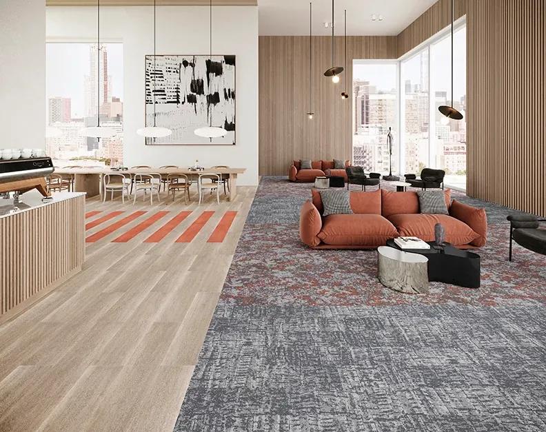 Modern office lounge with a mix of light wood flooring and patterned carpet tiles, featuring orange and gray tones