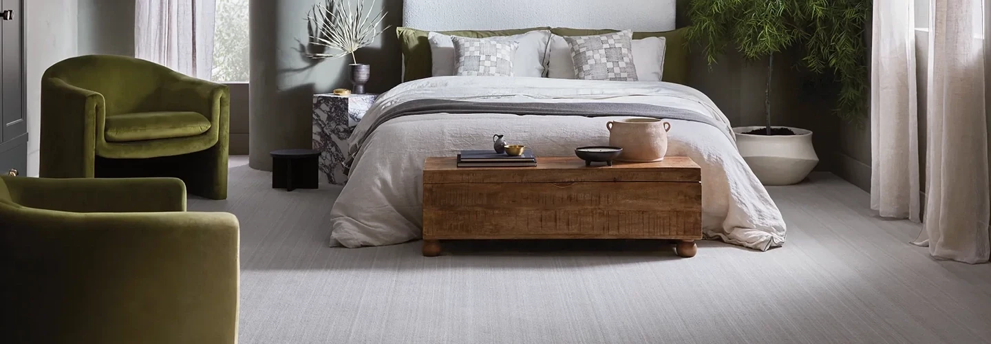 Modern bedroom with light gray carpet flooring, green velvet chairs, and wooden coffee table