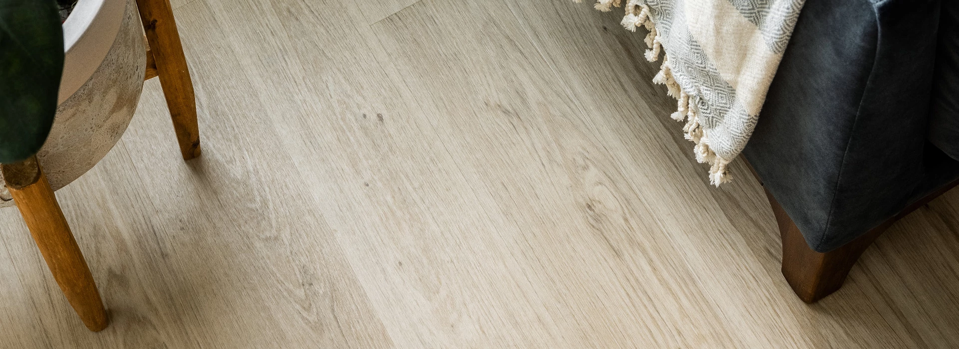 Light wood flooring in a cozy living room with a black leather sofa and a wooden side table