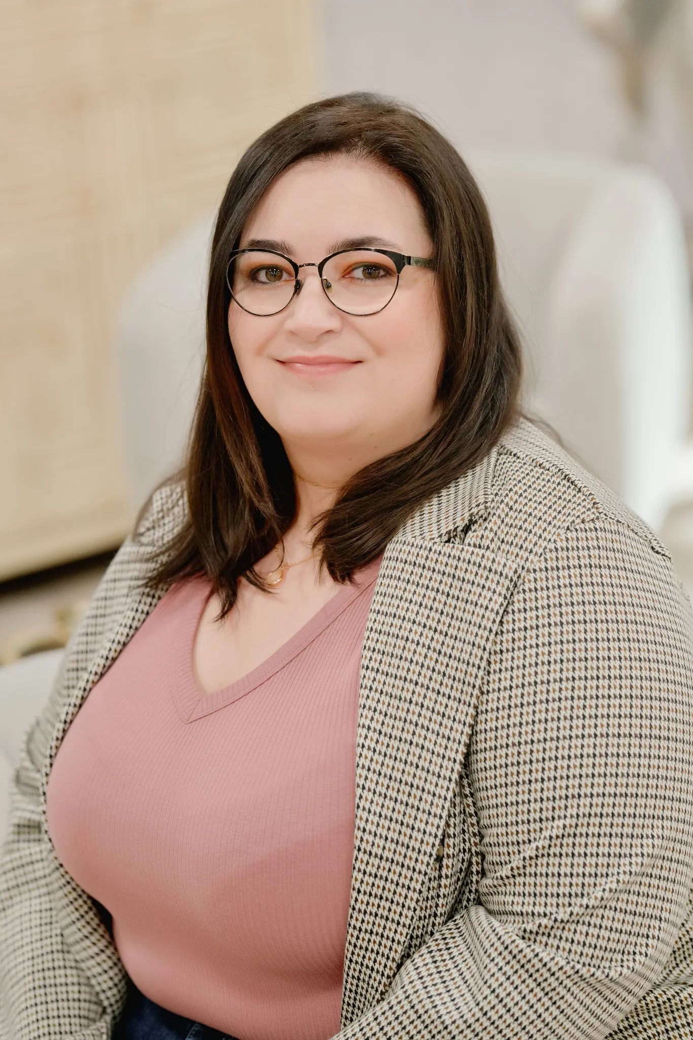 Woman in a pink top and checkered blazer sitting in a room with light-colored furniture