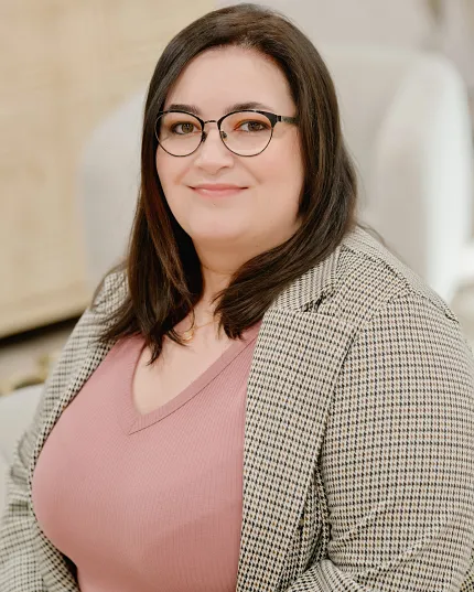 Woman in a pink top and checkered blazer in a modern room setting Woman in a pink top and checkered blazer sitting in a room with light-colored furniture
