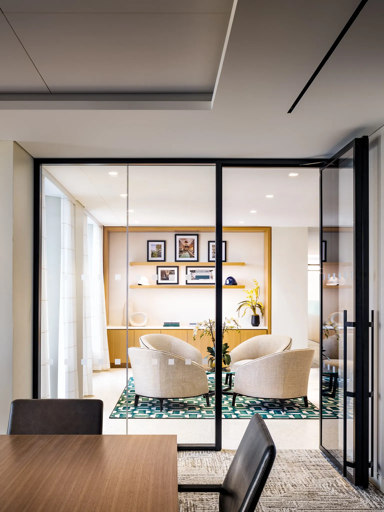 Modern workplace interior with glass partitions, beige armchairs, and a patterned green rug