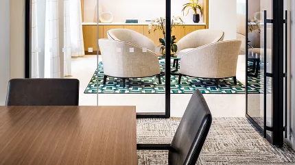 Contemporary Workplace Design with Glass Partitions and Stylish Furnishings Modern workplace interior with glass partitions, beige armchairs, and a patterned green rug