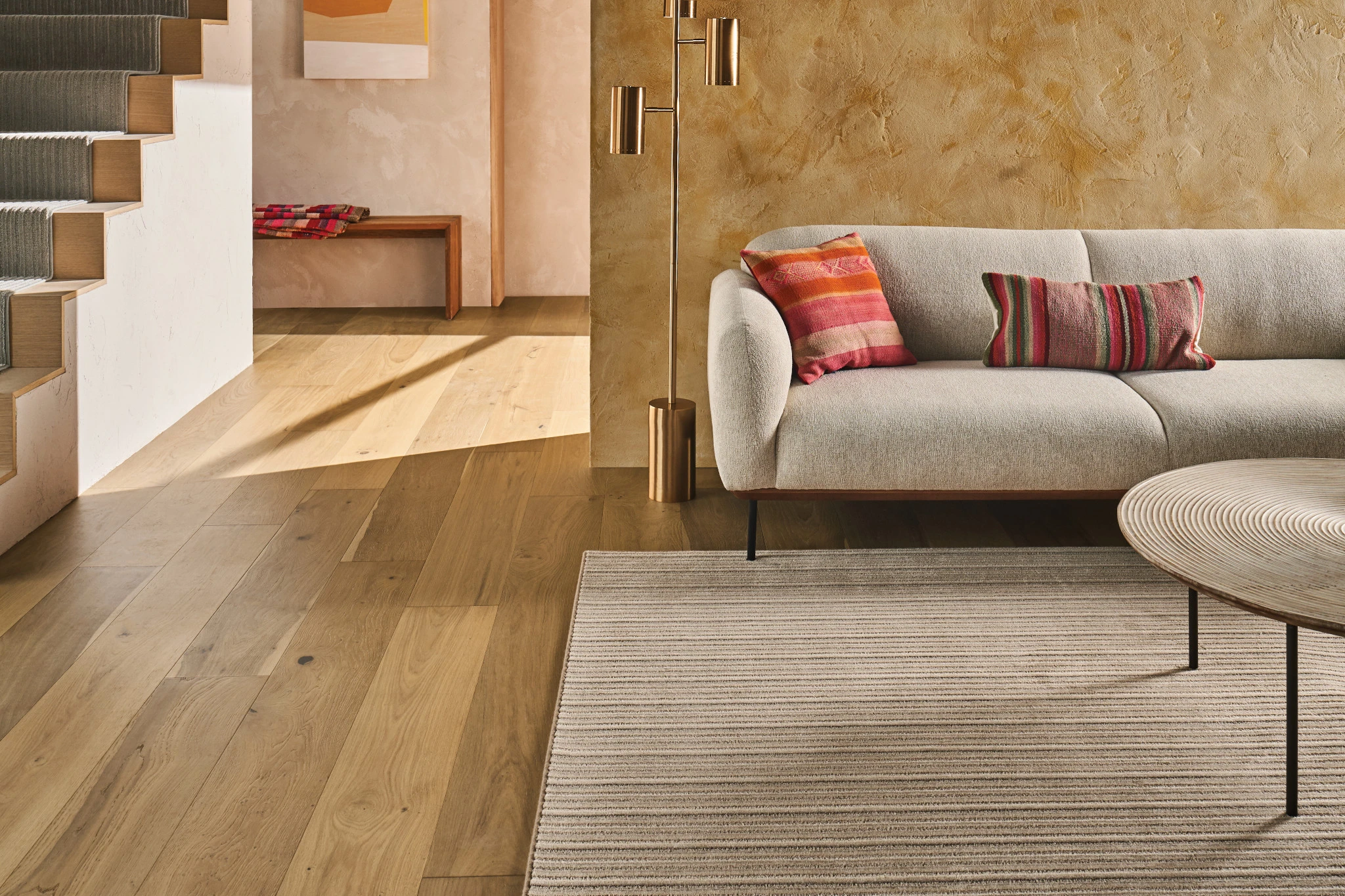 Modern living room with light hardwood flooring, beige sofa with colorful pillows, and a striped area rug