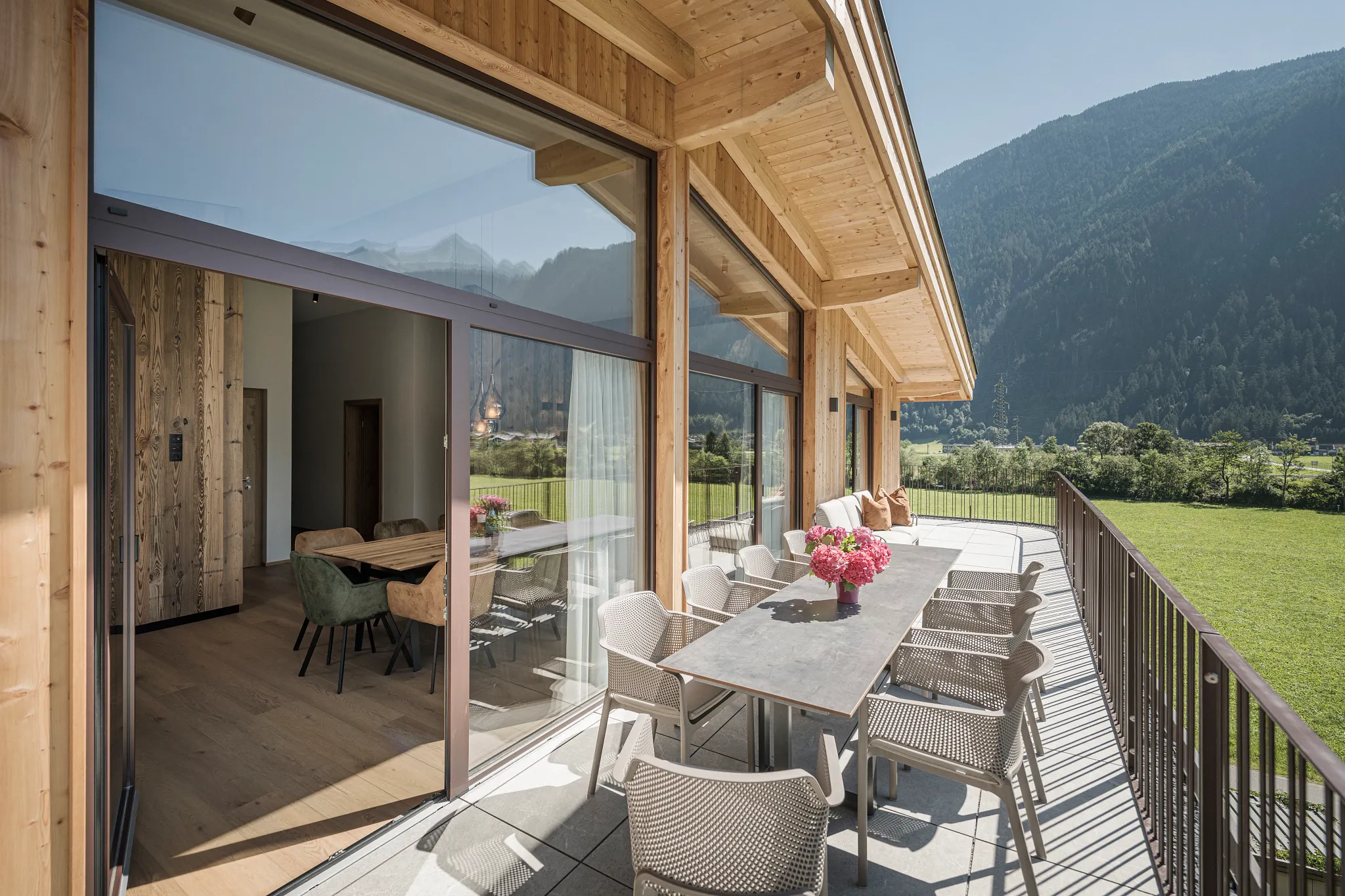 A terrace on a grassy field with sliding windows and a living area with oak flooring 