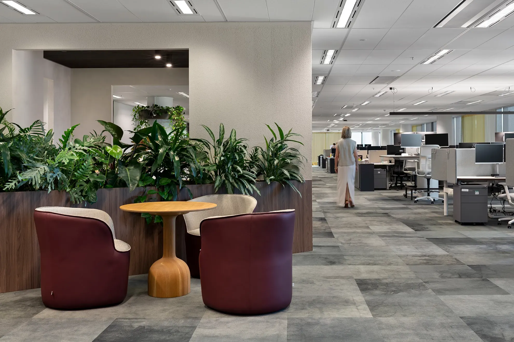 Modern workplace with commercial carpet tile flooring in shades of gray, featuring burgundy chairs and a wooden table surrounded by greenery