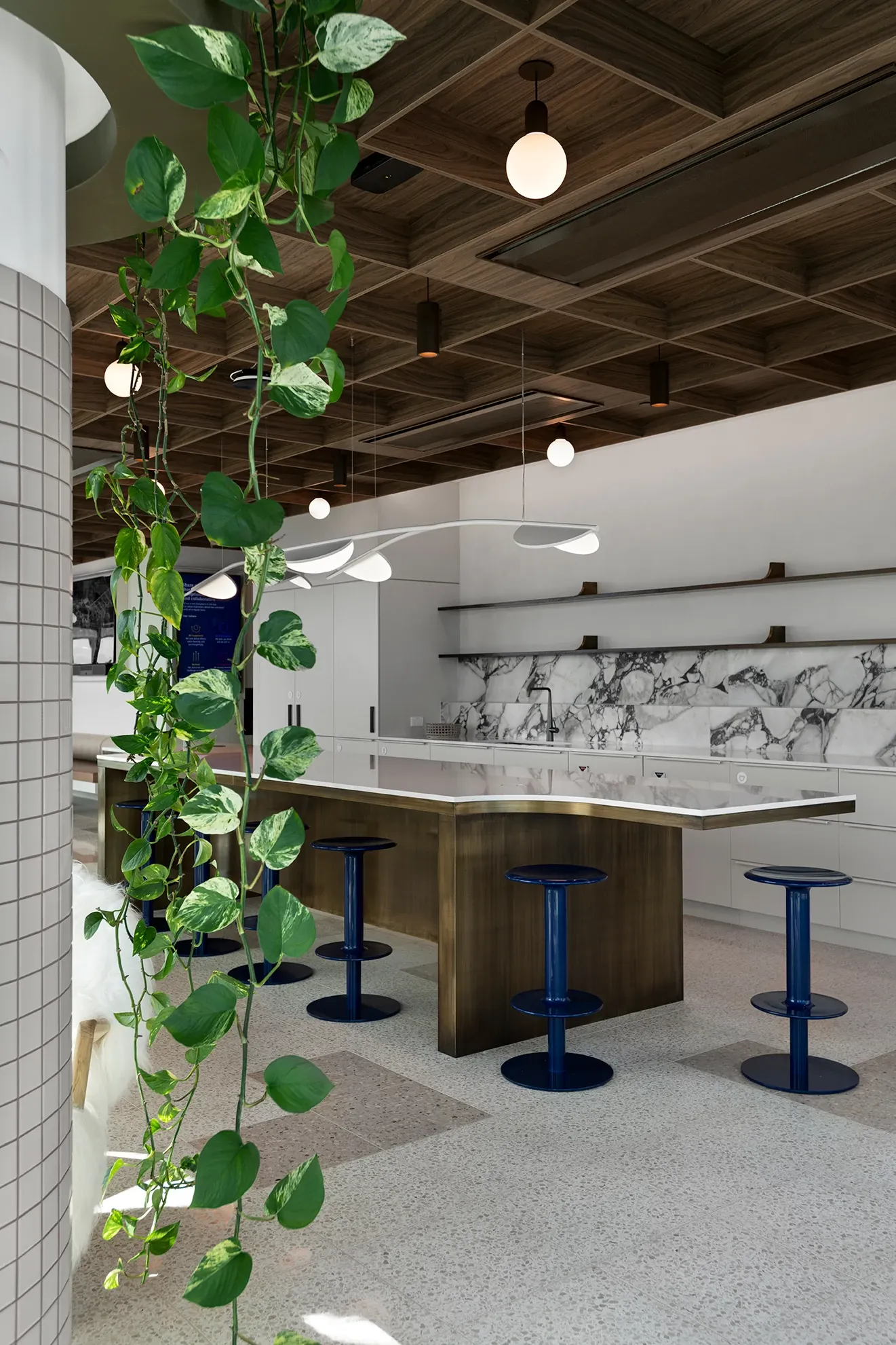 Modern kitchen area with terrazzo flooring, wooden ceiling, and blue bar stools