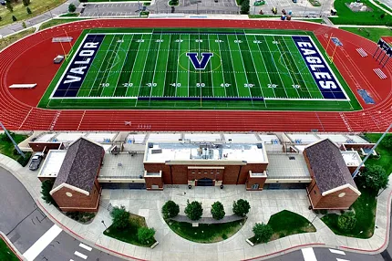 Artificial Turf Football Field with Running Track and Buildings - Aerial View Aerial view of a sports complex featuring an artificial turf football field with "Valor" and "Eagles" markings