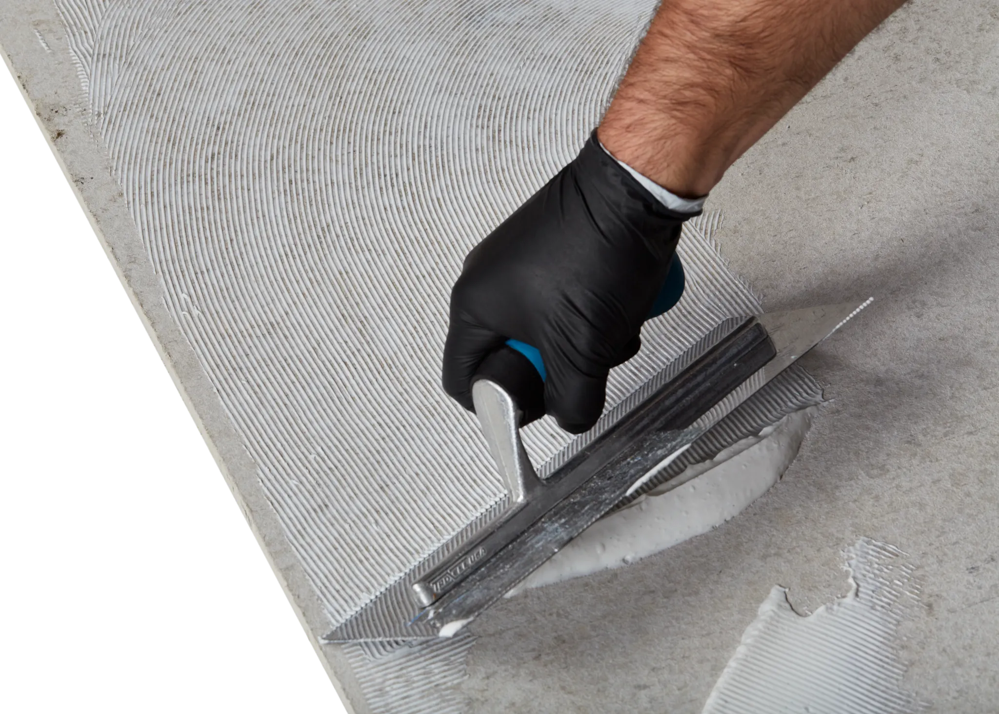 Close-up of a hand in a black glove using a trowel to apply adhesive on a concrete surface for flooring installation