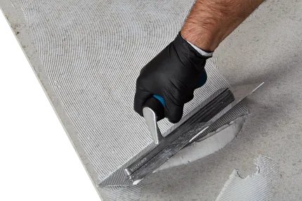 Flooring installation process with adhesive application using a trowel Close-up of a hand in a black glove using a trowel to apply adhesive on a concrete surface for flooring installation