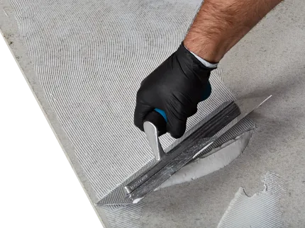 Flooring installation process with adhesive application using a trowel Close-up of a hand in a black glove using a trowel to apply adhesive on a concrete surface for flooring installation
