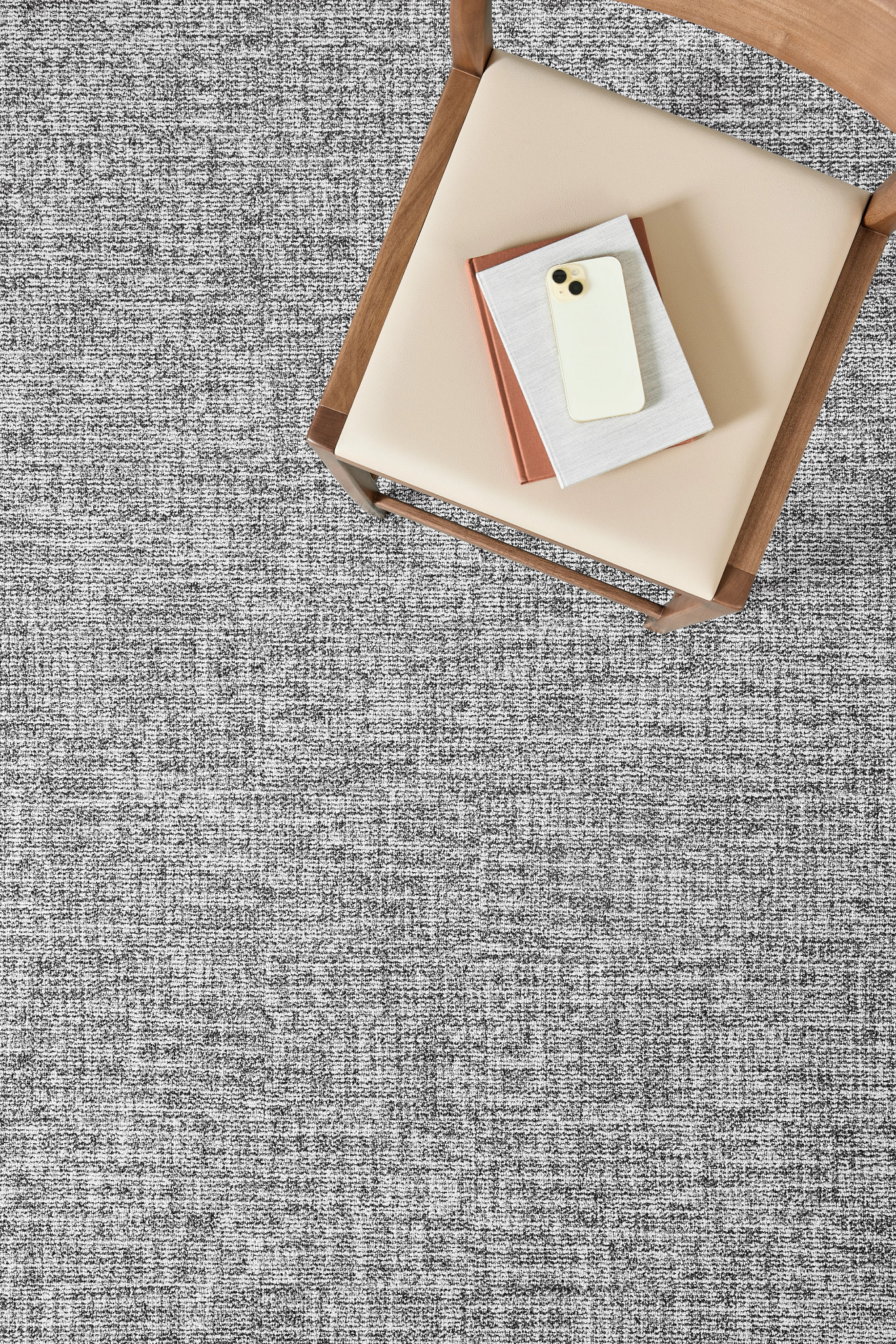 Top view of a beige chair with books and a smartphone on a textured gray commercial carpet tile