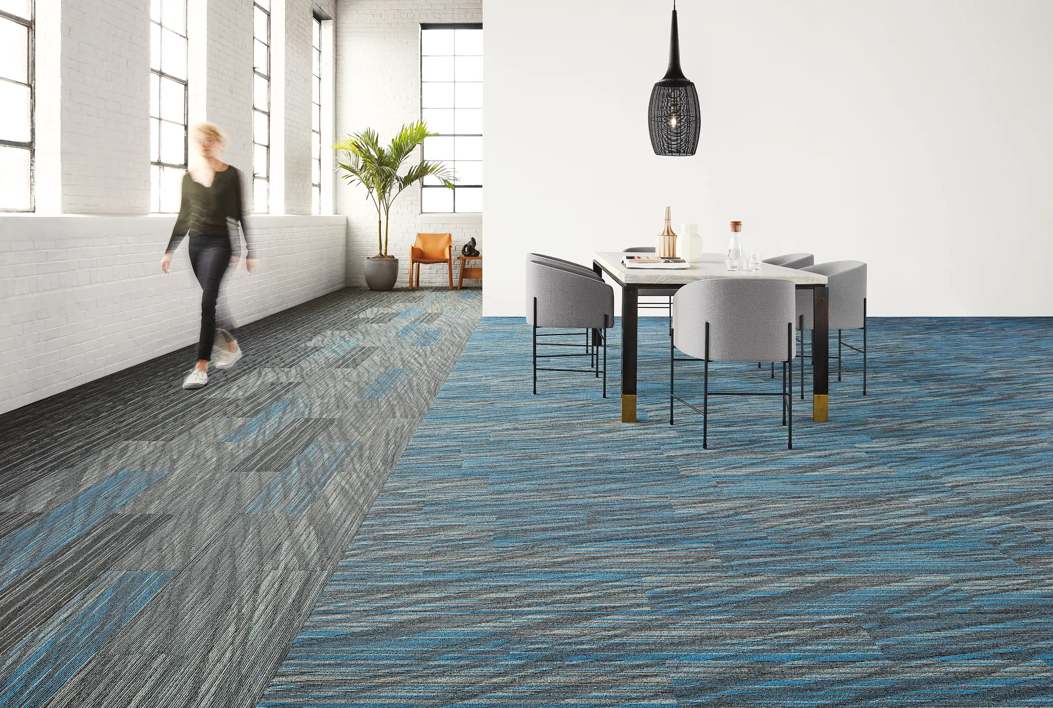 Modern office space with blue and gray commercial carpet tile flooring, featuring a woman walking and a meeting area with chairs and a table
