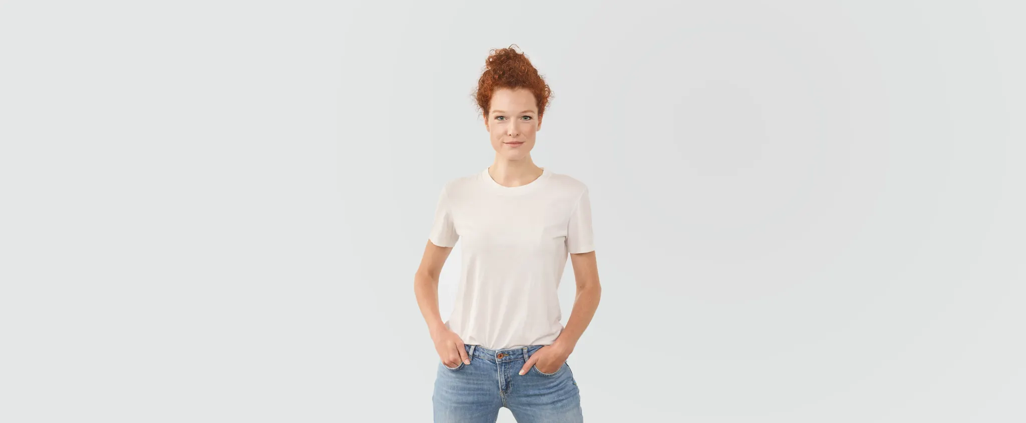 Young woman in casual white t-shirt and jeans standing against a plain background