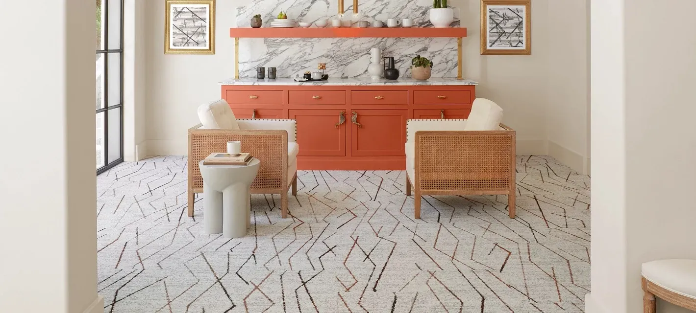 Modern living room with geometric patterned flooring, orange cabinetry, and wicker chairs