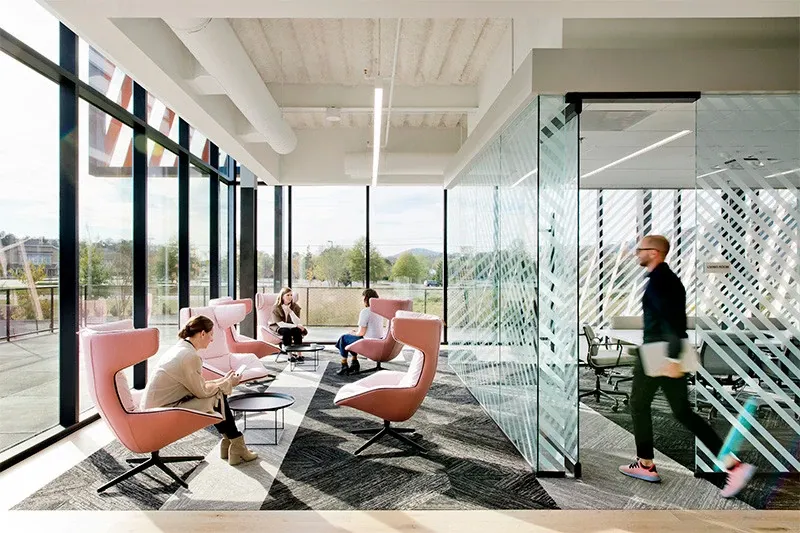 Modern workplace with large windows, pink chairs, and commercial carpet tile flooring