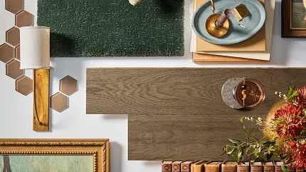Green carpet, brown laminate flooring, and hexagonal ceramic tiles in a homely setting. A cozy home setting featuring a green textured carpet swatch, a piece of brown wood-look laminate flooring, and hexagonal brown ceramic tiles, surrounded by vintage books and decor