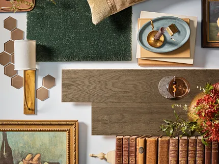 Green carpet, brown laminate flooring, and hexagonal ceramic tiles in a homely setting. A cozy home setting featuring a green textured carpet swatch, a piece of brown wood-look laminate flooring, and hexagonal brown ceramic tiles, surrounded by vintage books and decor