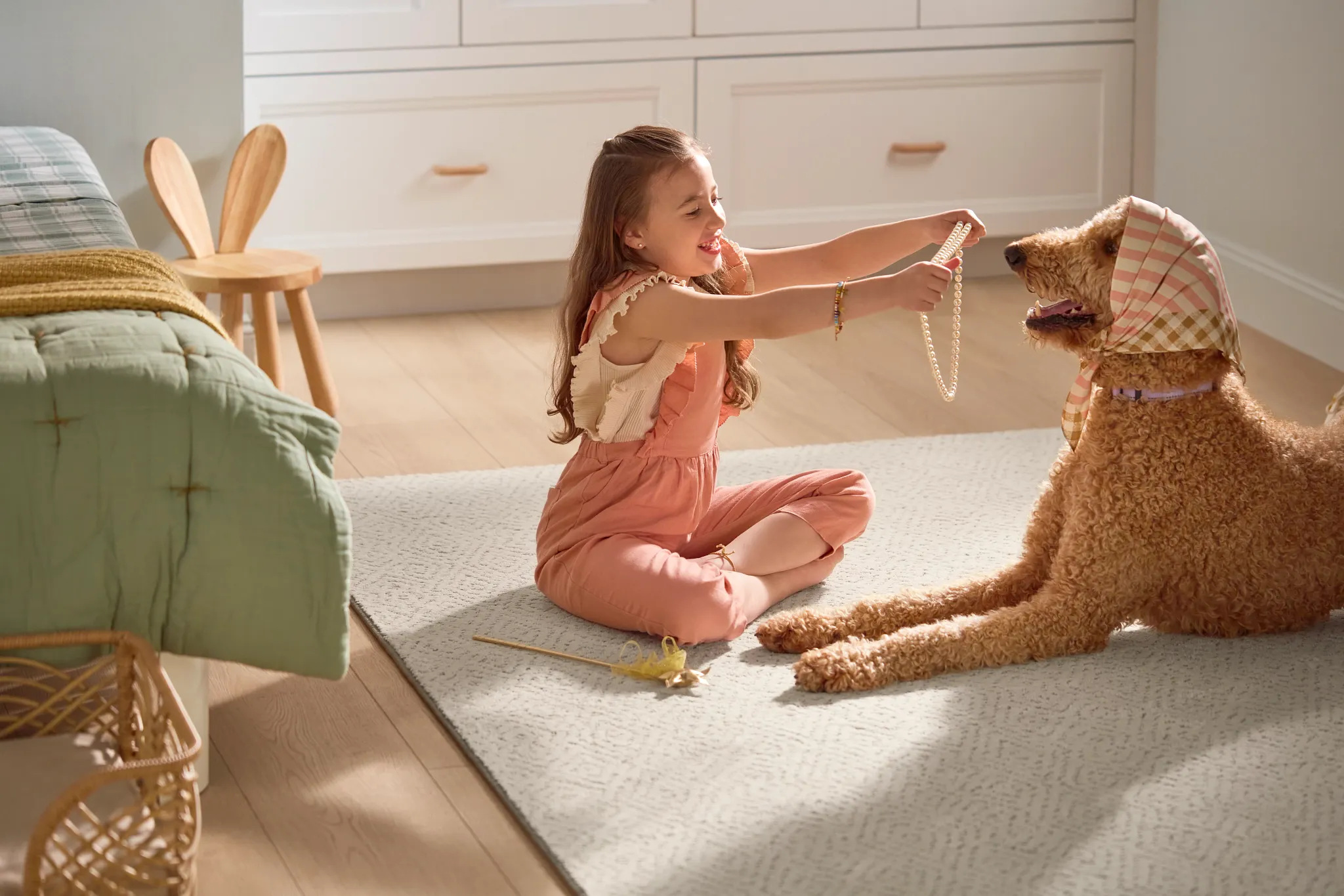 Cozy room scene with a young girl playing with a dog on a soft, patterned carpet, surrounded by light wood flooring and comfortable home furnishings
