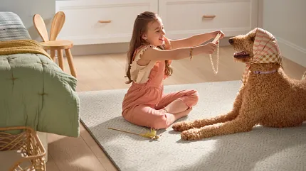 Comfortable and Durable Carpet for Everyday Home Comfort Cozy room scene with a young girl playing with a dog on a soft, patterned carpet, surrounded by light wood flooring and comfortable home furnishings