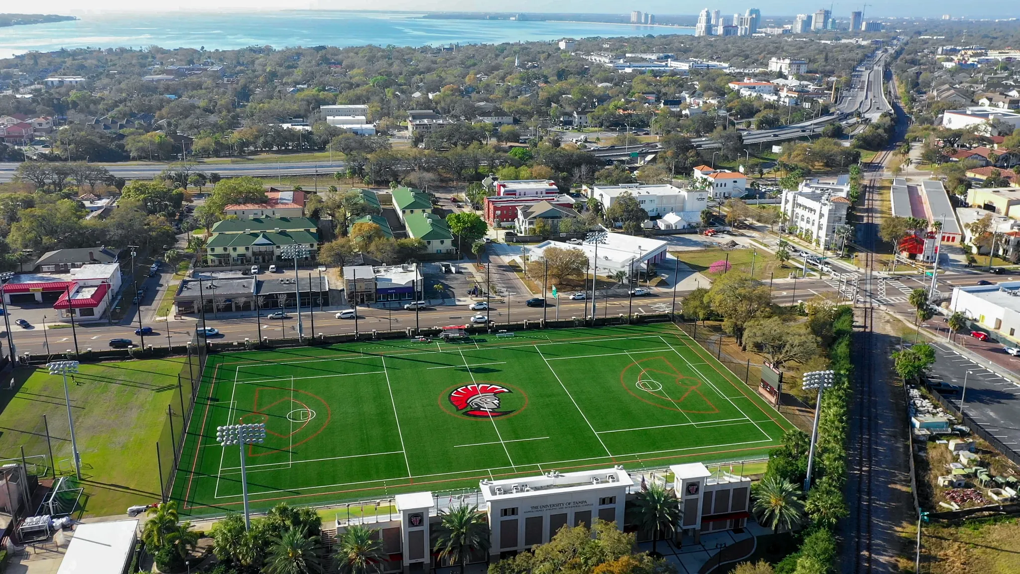 Aerial view of a sports field with artificial turf surrounded by urban landscape and buildings