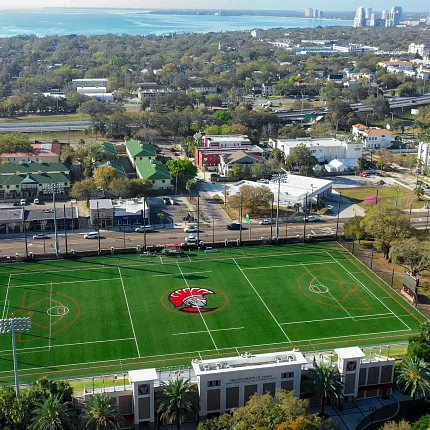 Aerial View of Sports Field with Artificial Turf in Urban Area Aerial view of a sports field with artificial turf surrounded by urban landscape and buildings
