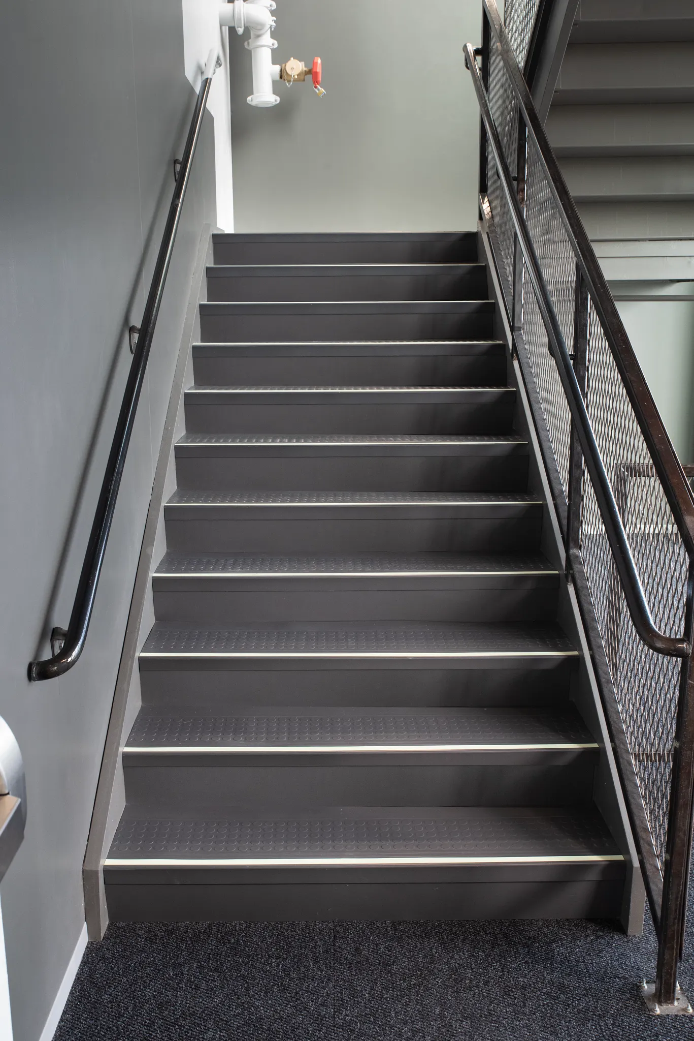 Industrial staircase with gray anti-slip flooring and black handrails