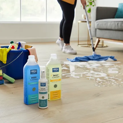 Light Wood Look LVP Flooring Cleaning Scene with COREtec Products Woman cleaning light wood look luxury vinyl plank flooring with cleaning products in a bright living room