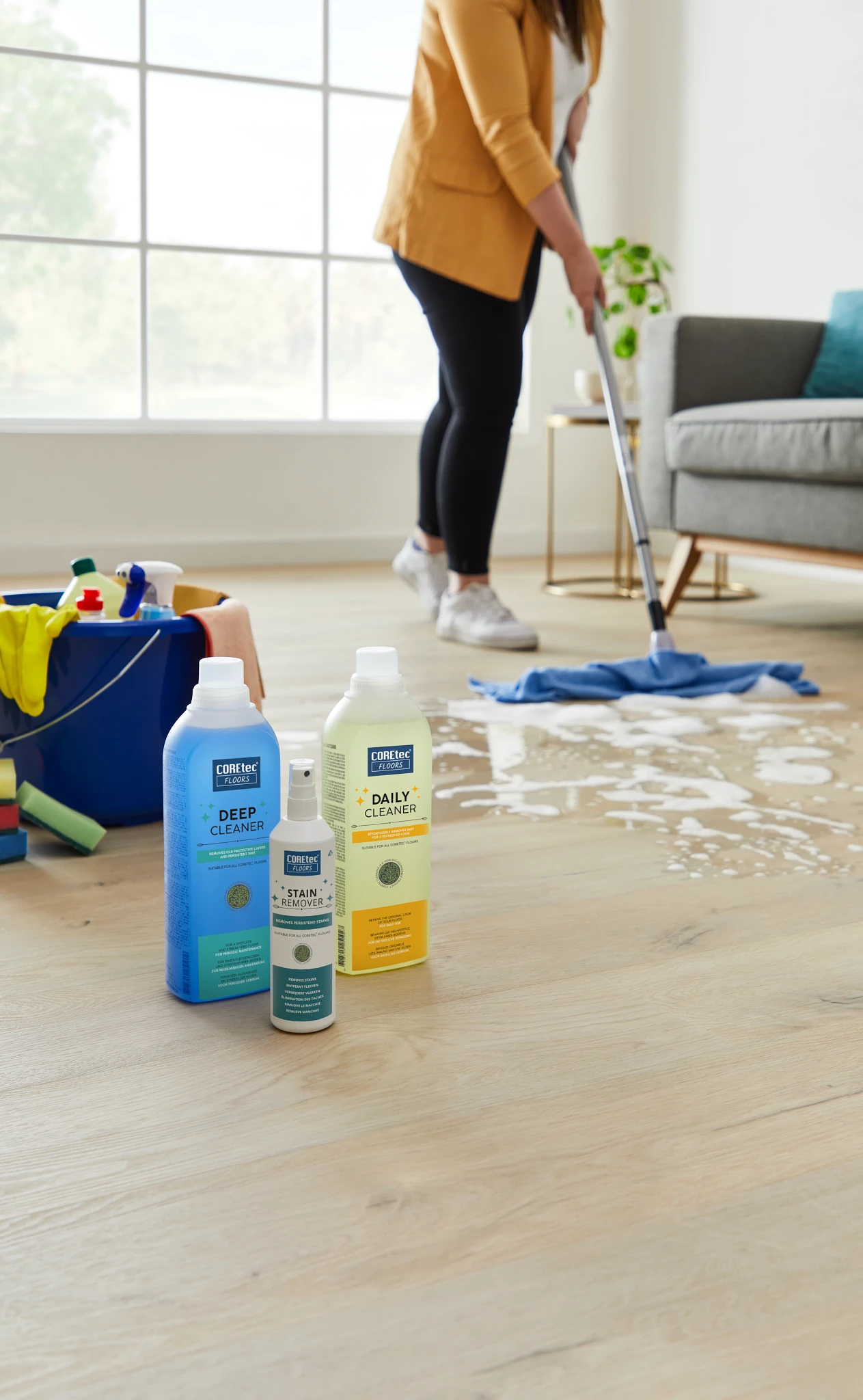 Light Wood Look LVP Flooring Cleaning Scene with COREtec Products Woman cleaning light wood look luxury vinyl plank flooring with cleaning products in a bright living room