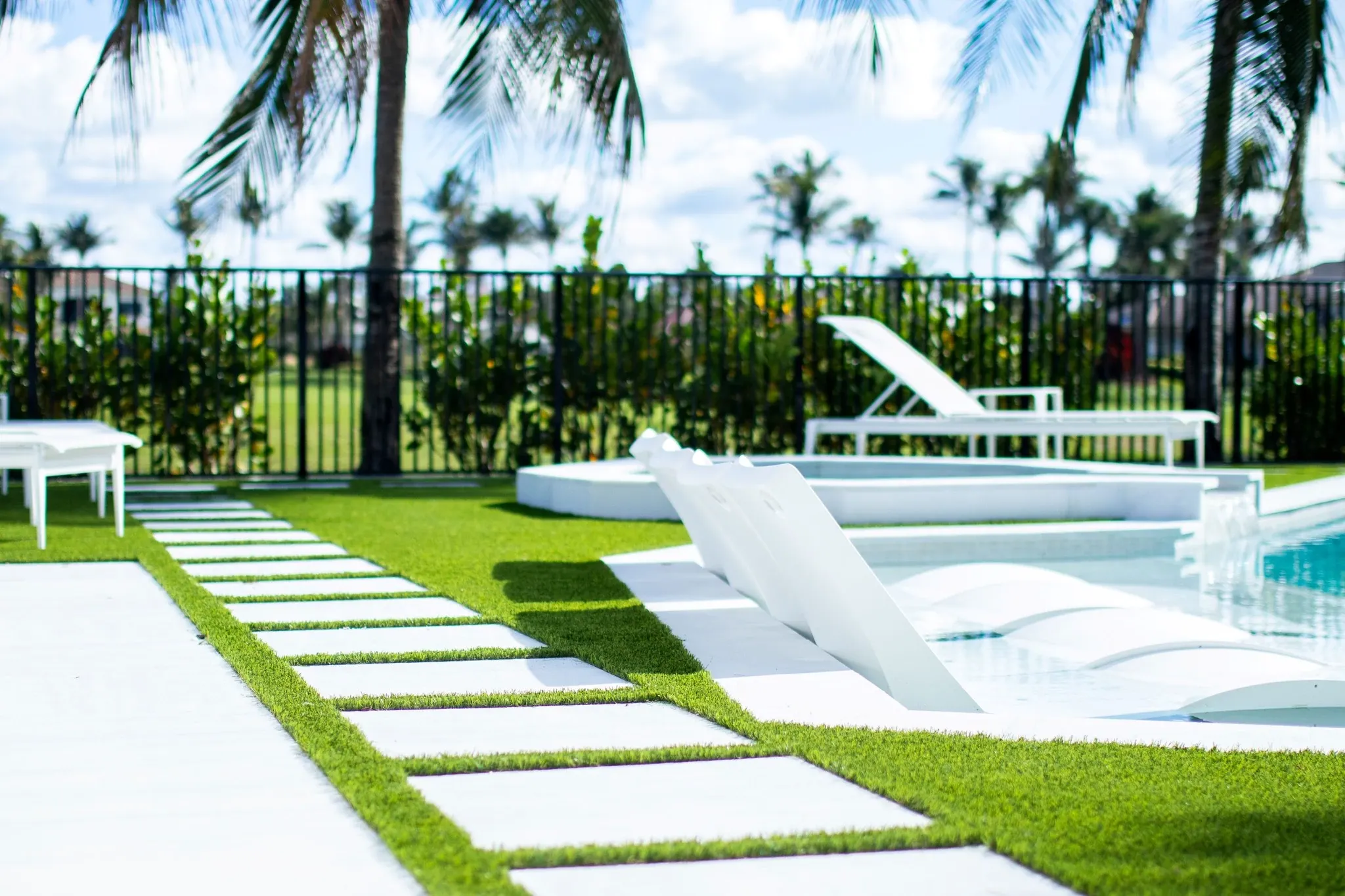 Modern outdoor pool area with white lounge chairs and green grass