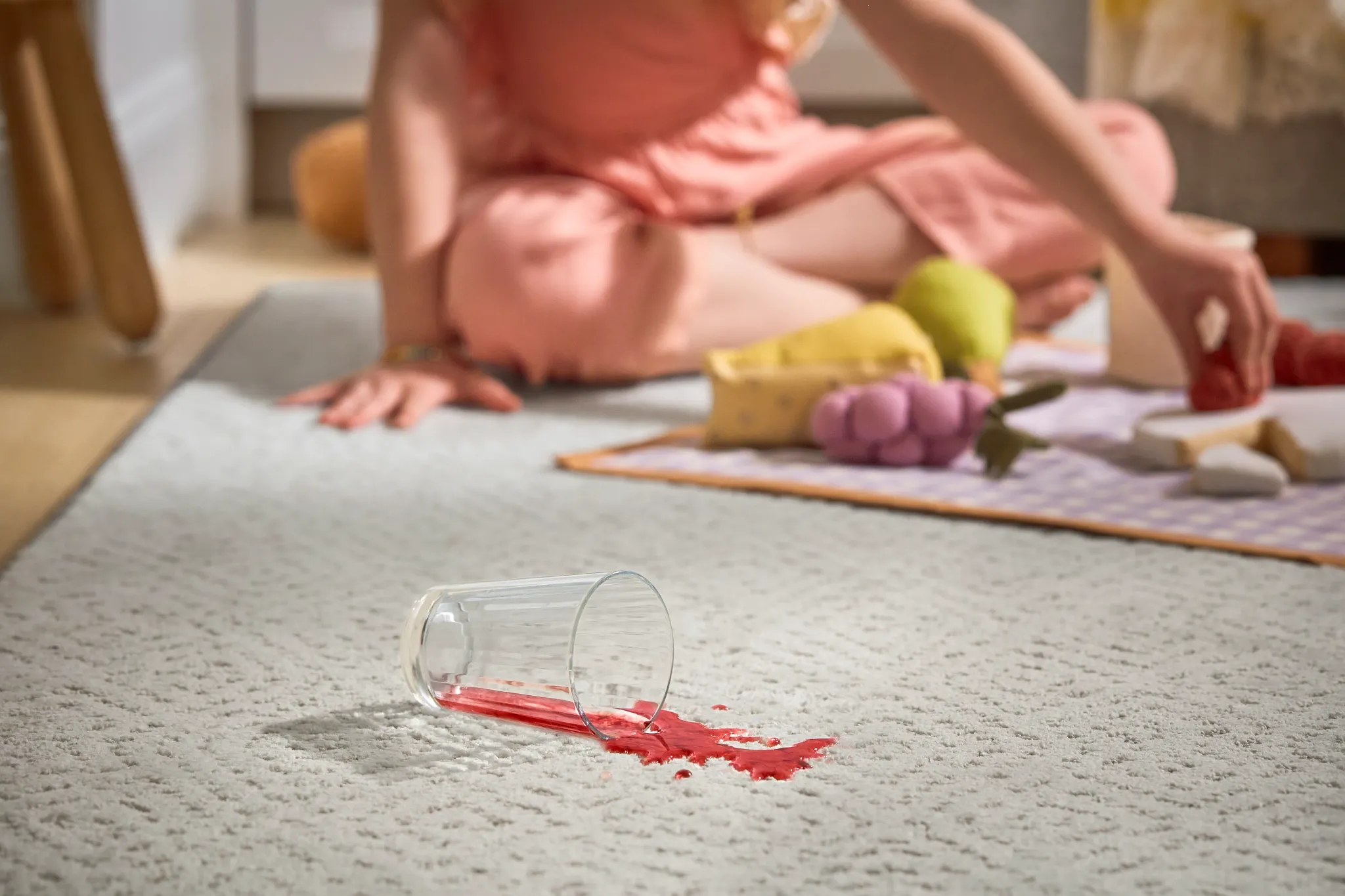 Woman in a peach dress sitting on a light gray carpet with a spilled red drink, showcasing the carpet's stain-resistant and easy-to-clean features