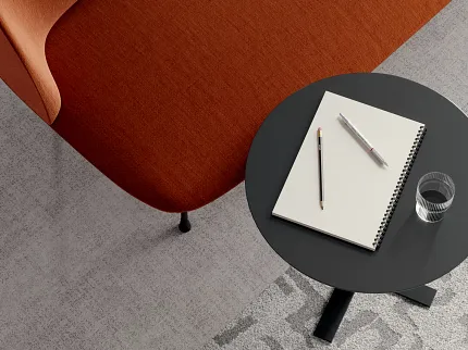 Contemporary office space with commercial carpet tile flooring and stylish furniture Modern office setting with a red-orange chair and a black round table on light gray commercial carpet tile