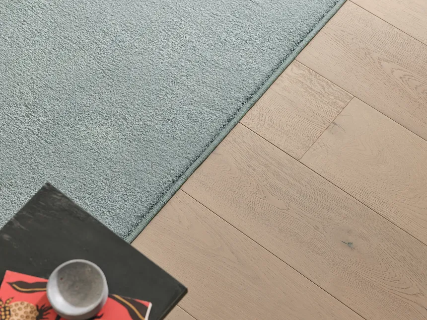 Light Blue Synthetic Carpet on Wooden Floor Scene Light blue synthetic carpet on wooden floor with a black table and cup