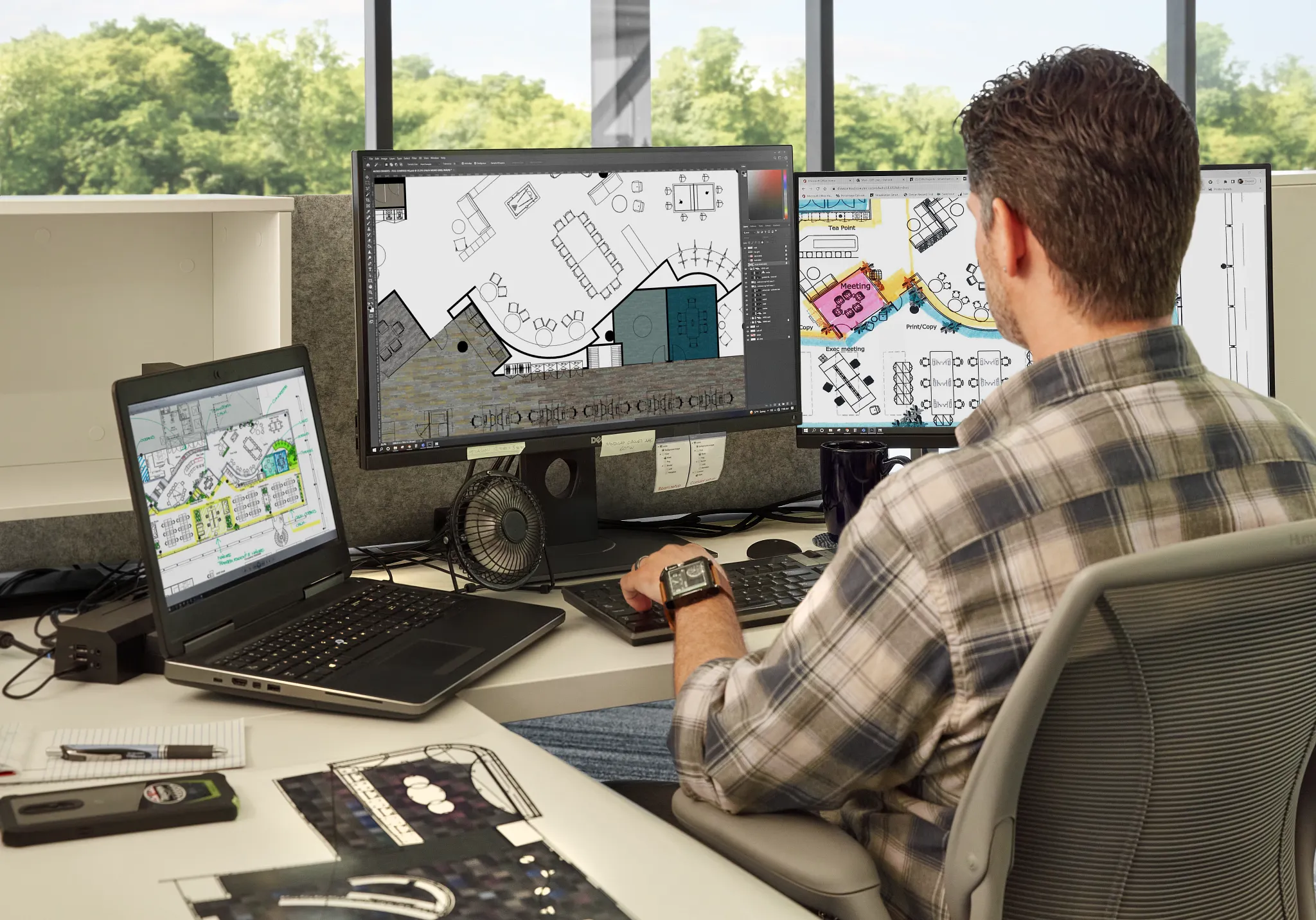 Man working at a desk with multiple computer screens displaying architectural designs in a modern office setting