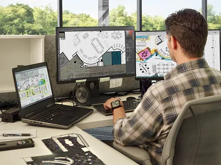 Office workspace with architectural design software on screens Man working at a desk with multiple computer screens displaying architectural designs in a modern office setting