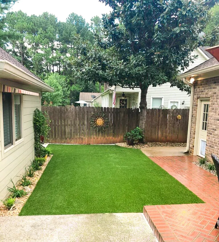 Compact residential backyard with freshly installed artificial turf lawn bordered by brick patio and wooden privacy fence.
