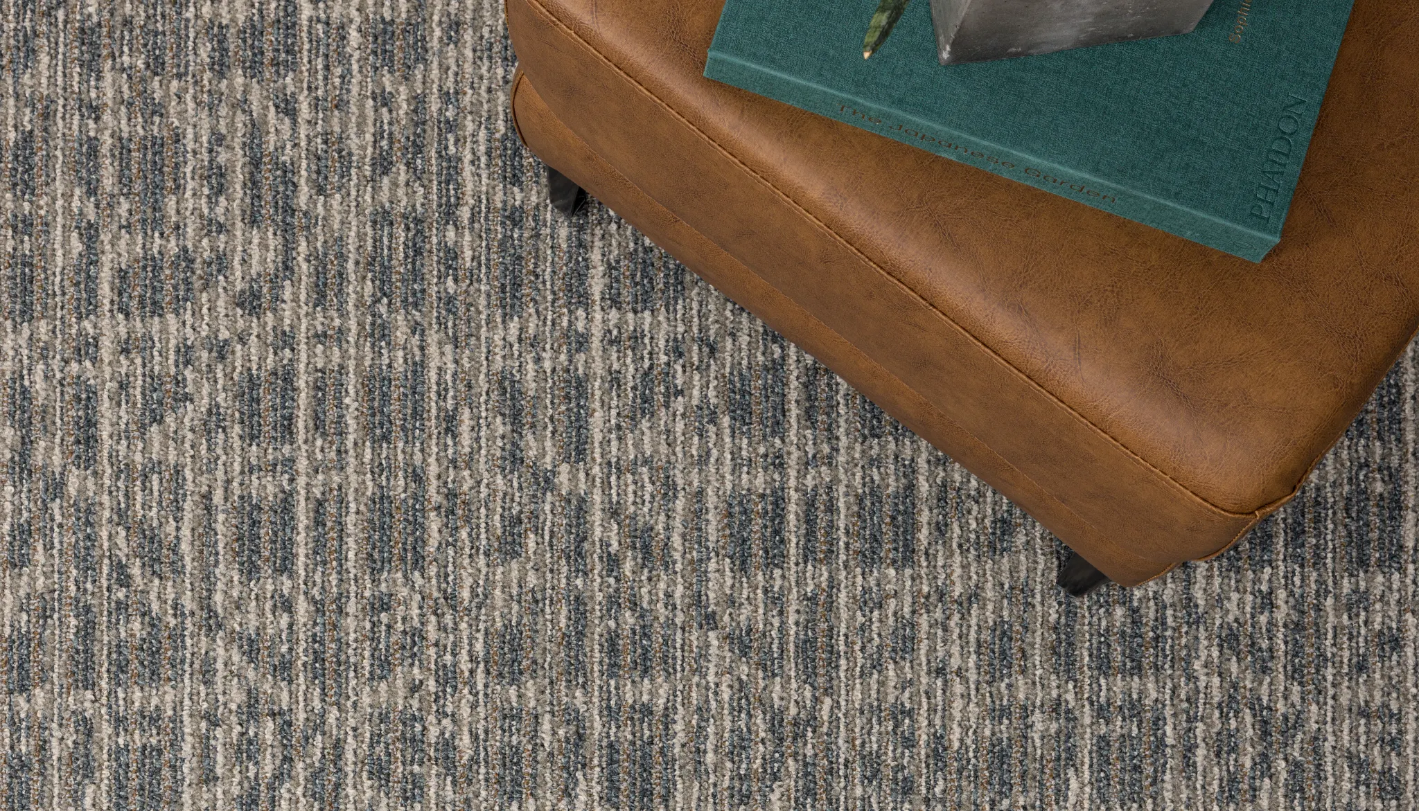Commercial Broadloom Carpet in blue and beige pattern with a brown leather ottoman and a plant on a book