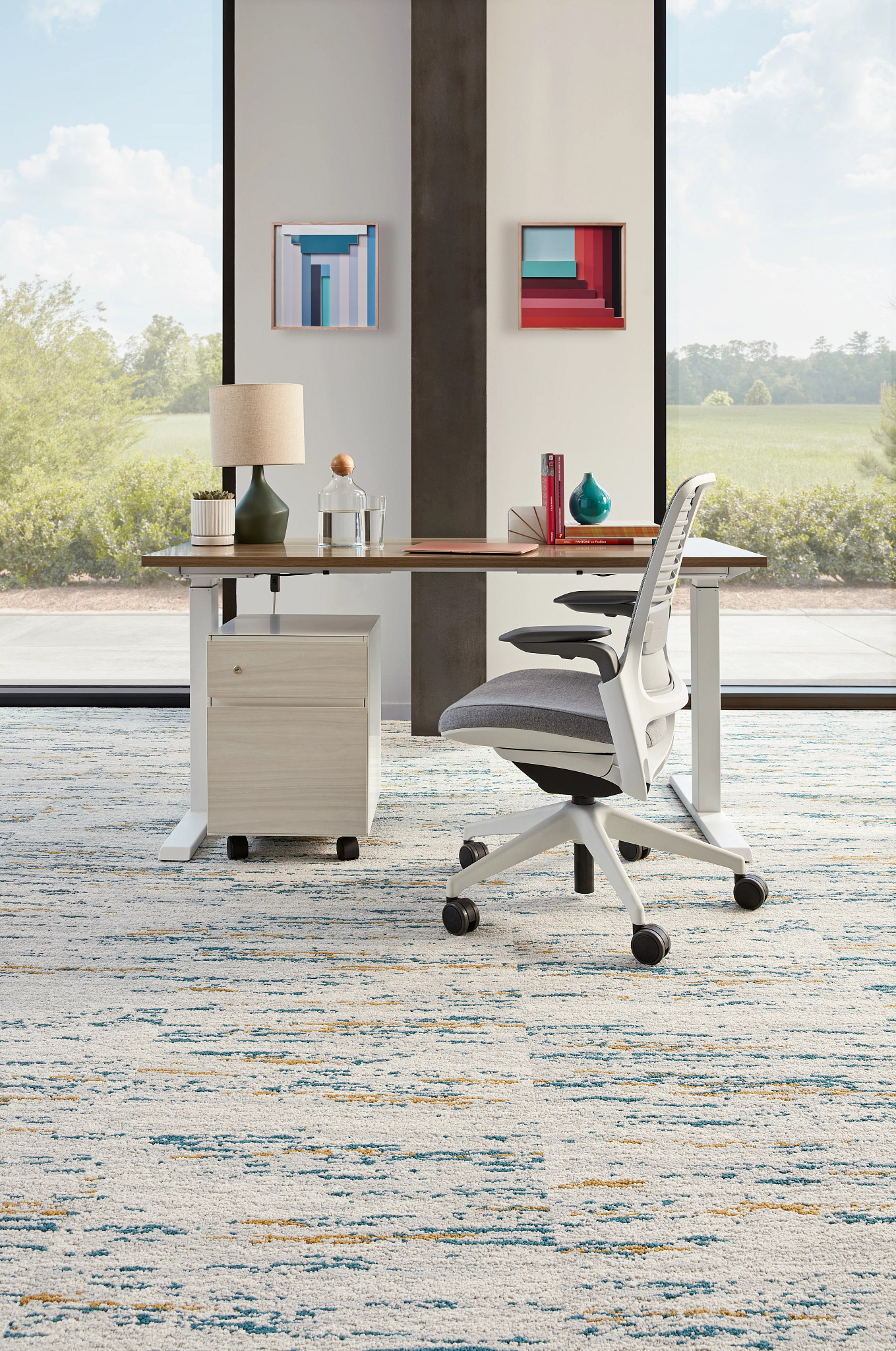 Modern office space with a white and gray ergonomic chair, wooden desk, and abstract art on the walls, featuring a textured commercial carpet tile in shades of blue, gray, and beige