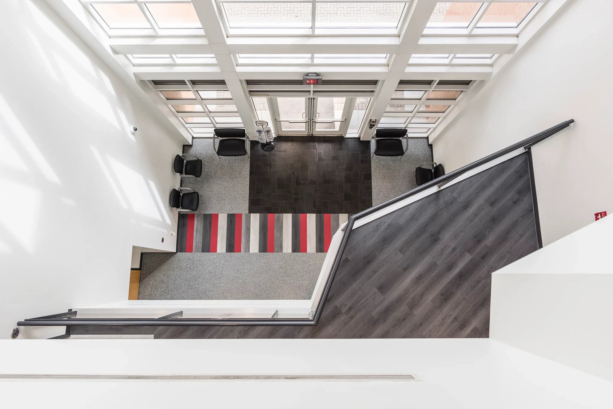 Overhead view of an education facility lobby featuring a mix of dark wood flooring, gray carpet tiles, and a striped red, gray, and white carpet runner