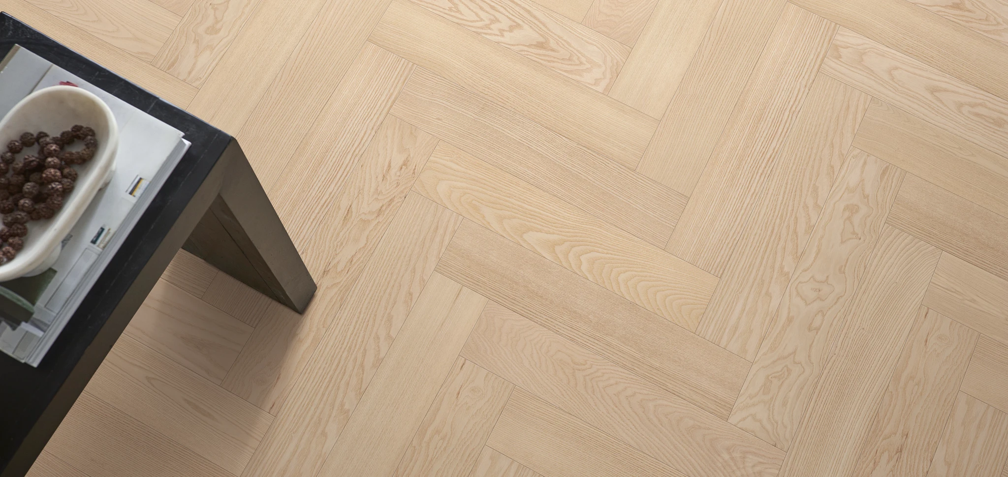 Light wood herringbone hardwood flooring with a black table and decorative bowl