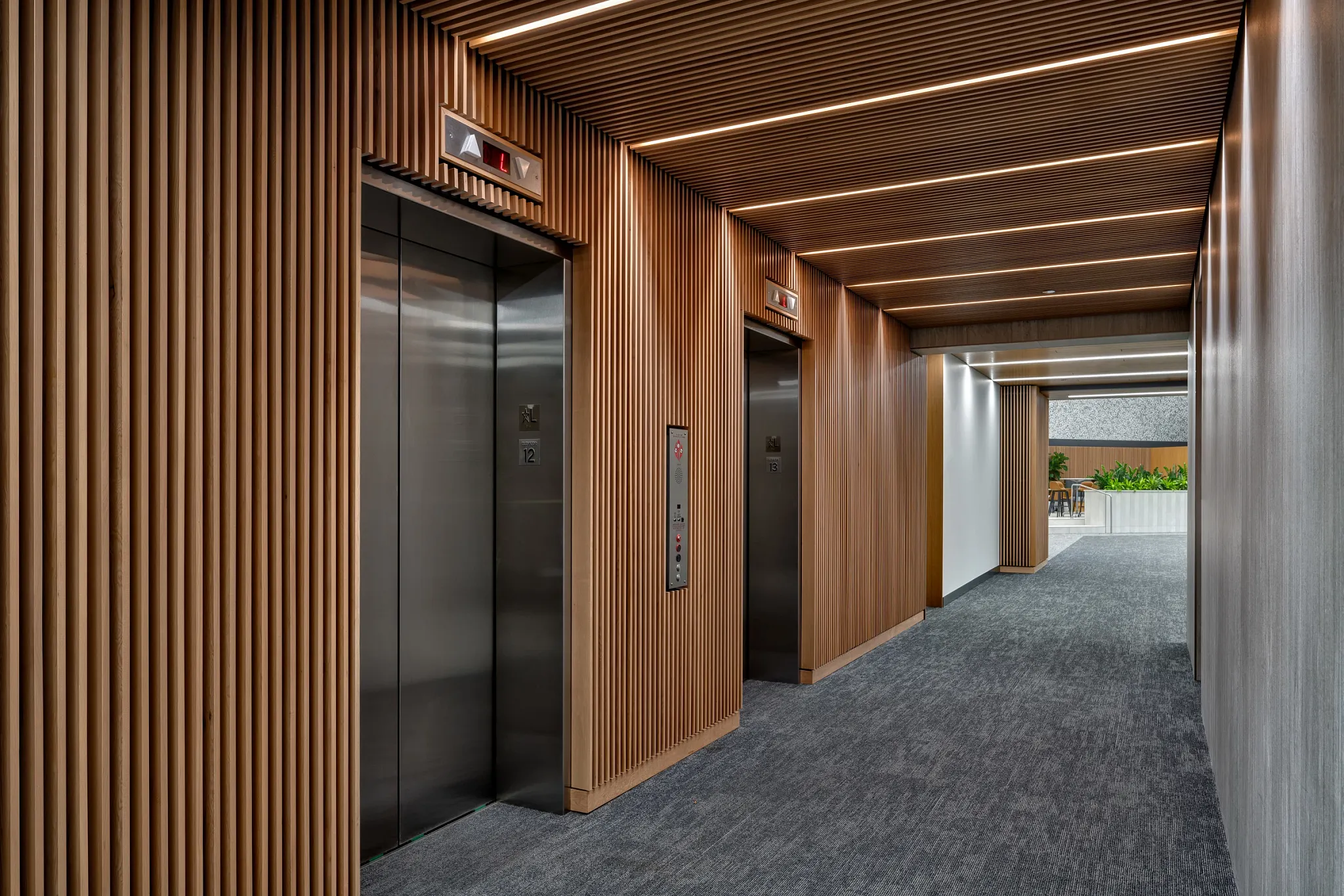 Modern workplace entryway with 24x24 inch commercial carpet tile flooring, featuring sleek elevators and wooden paneling.