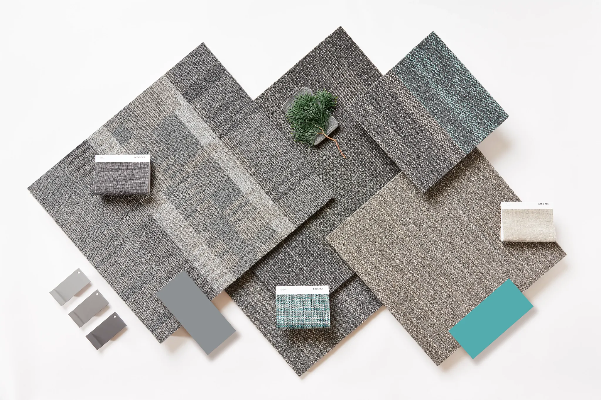 Swatch of commercial carpet tiles in shades of gray, beige, and teal with texture variations