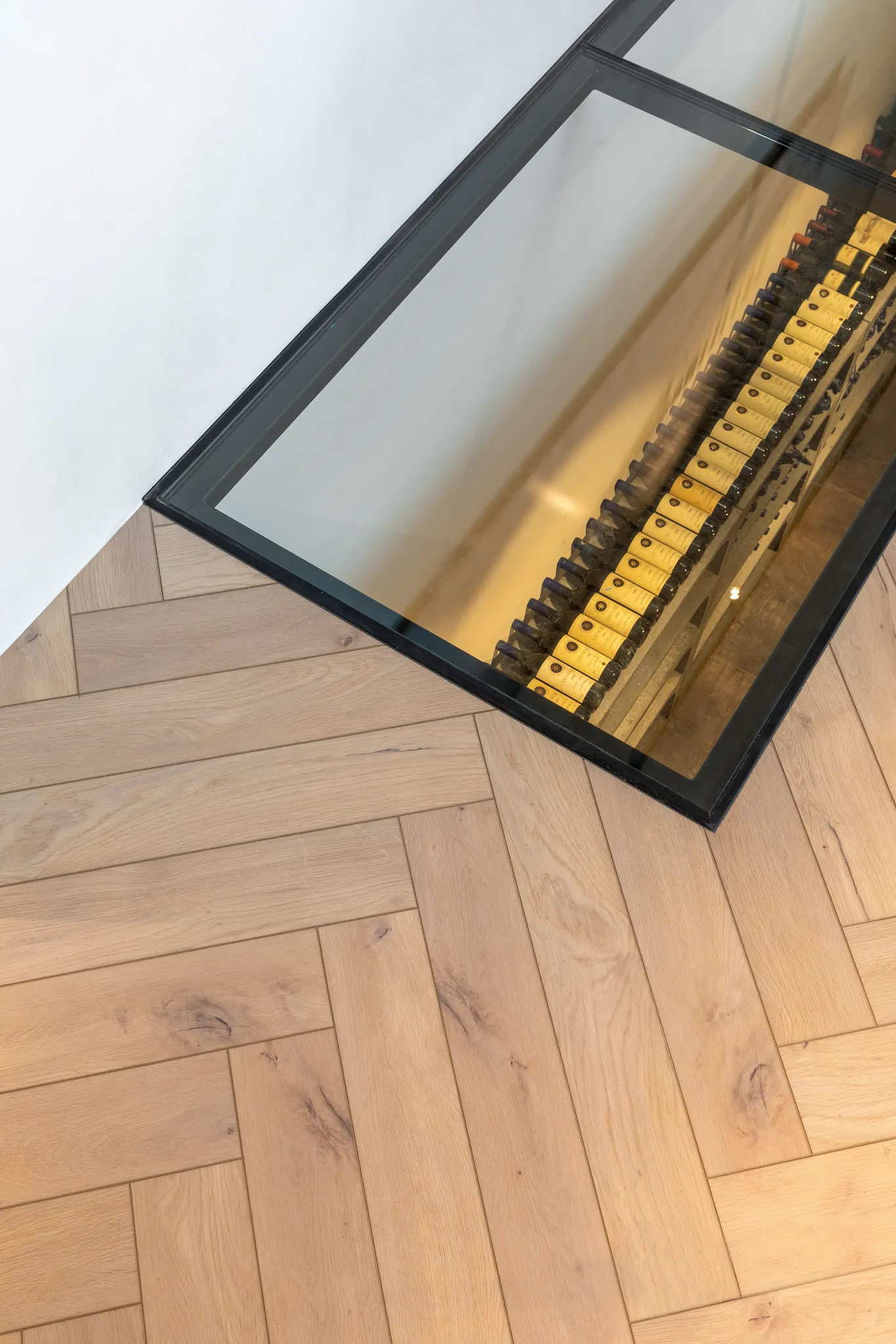 Light oak herringbone flooring with glass wine cellar view