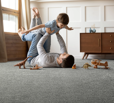 A father playing airplane with his son in a carpeted kids room.