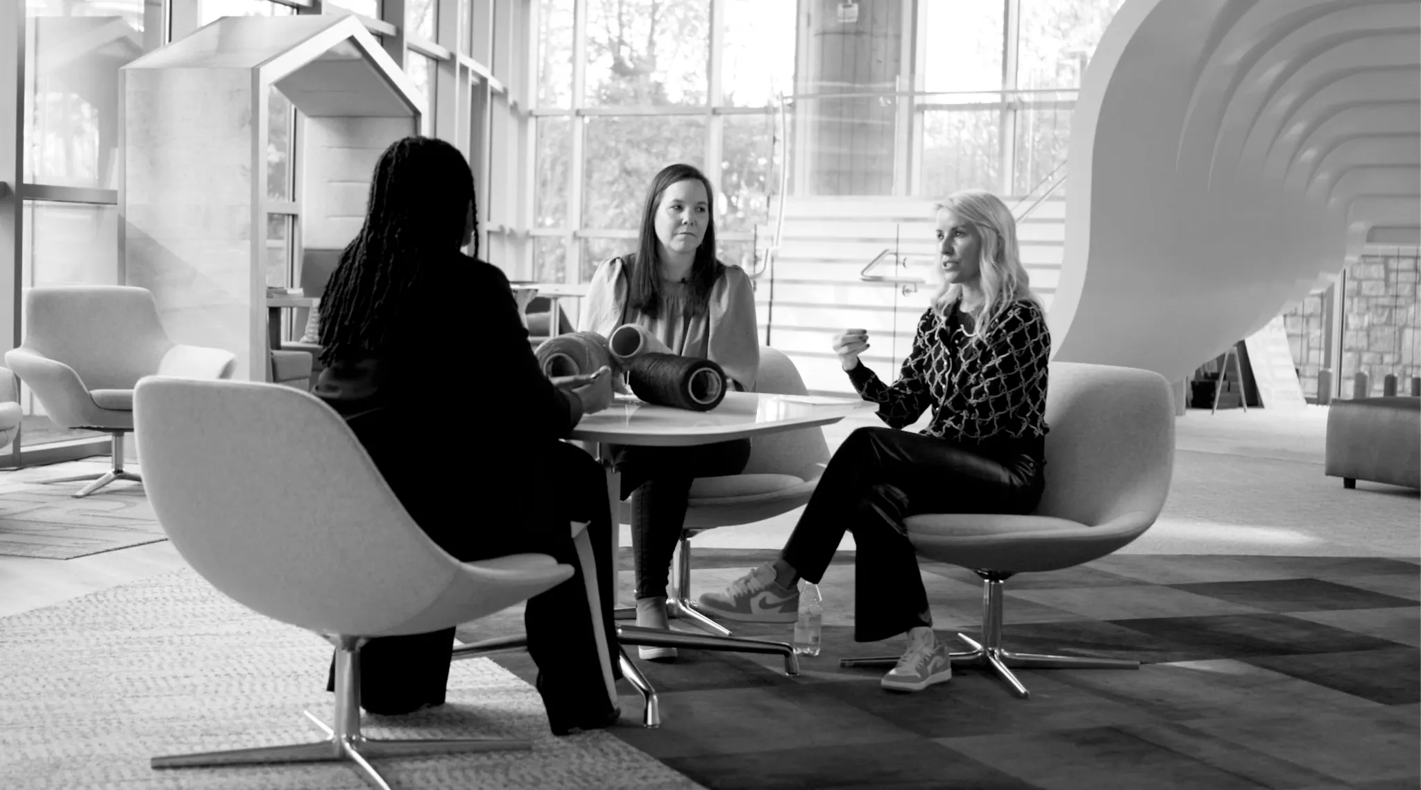 Modern education facility with three women seated on contemporary chairs, discussing over a table with commercial carpet tile flooring