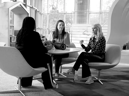 Education Facility with Commercial Carpet Tile Flooring and Modern Seating Arrangement Modern education facility with three women seated on contemporary chairs, discussing over a table with commercial carpet tile flooring