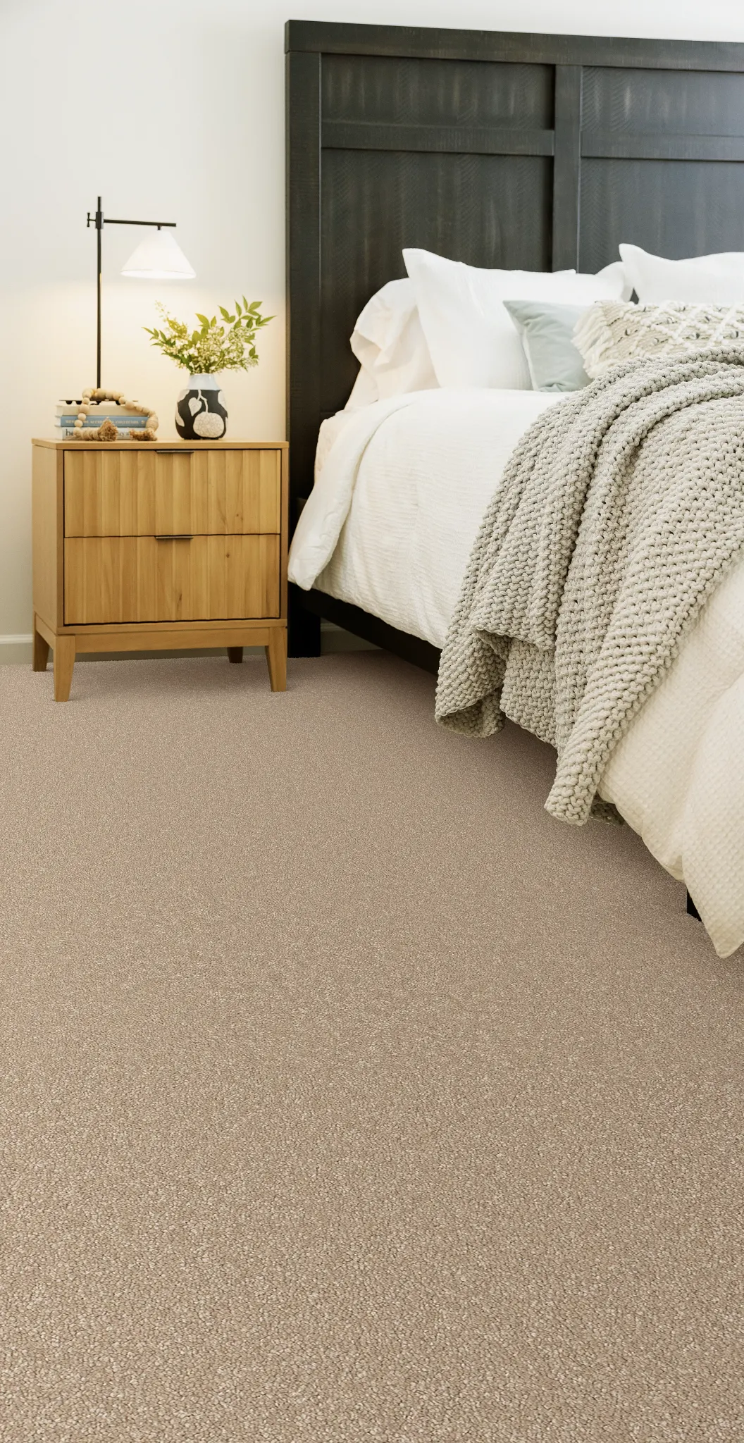 Cozy bedroom with beige carpet flooring, wooden nightstand, and dark headboard
