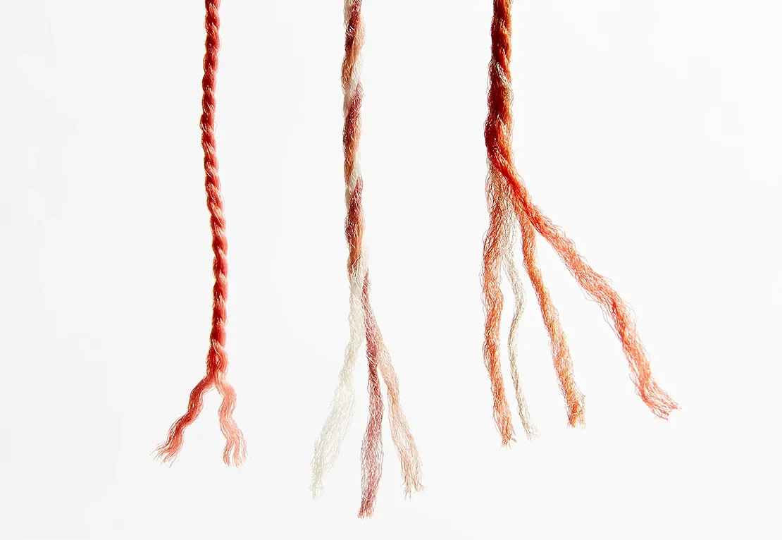 Close-up of three twisted yarn strands in shades of red, beige, and orange on a white background